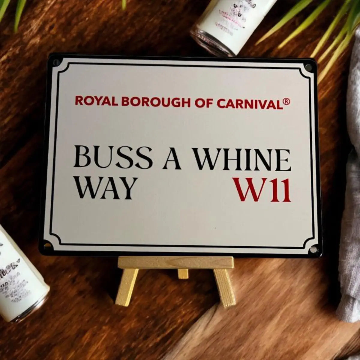Buss A Whine Way W11 decorative street sign styled flat on a wooden easel against rich wood grain and palm leaves