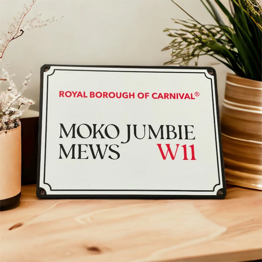 Moko Jumbie Mews W11 mini decorative street sign styled upright on a wooden table beside ceramic vases and foliage