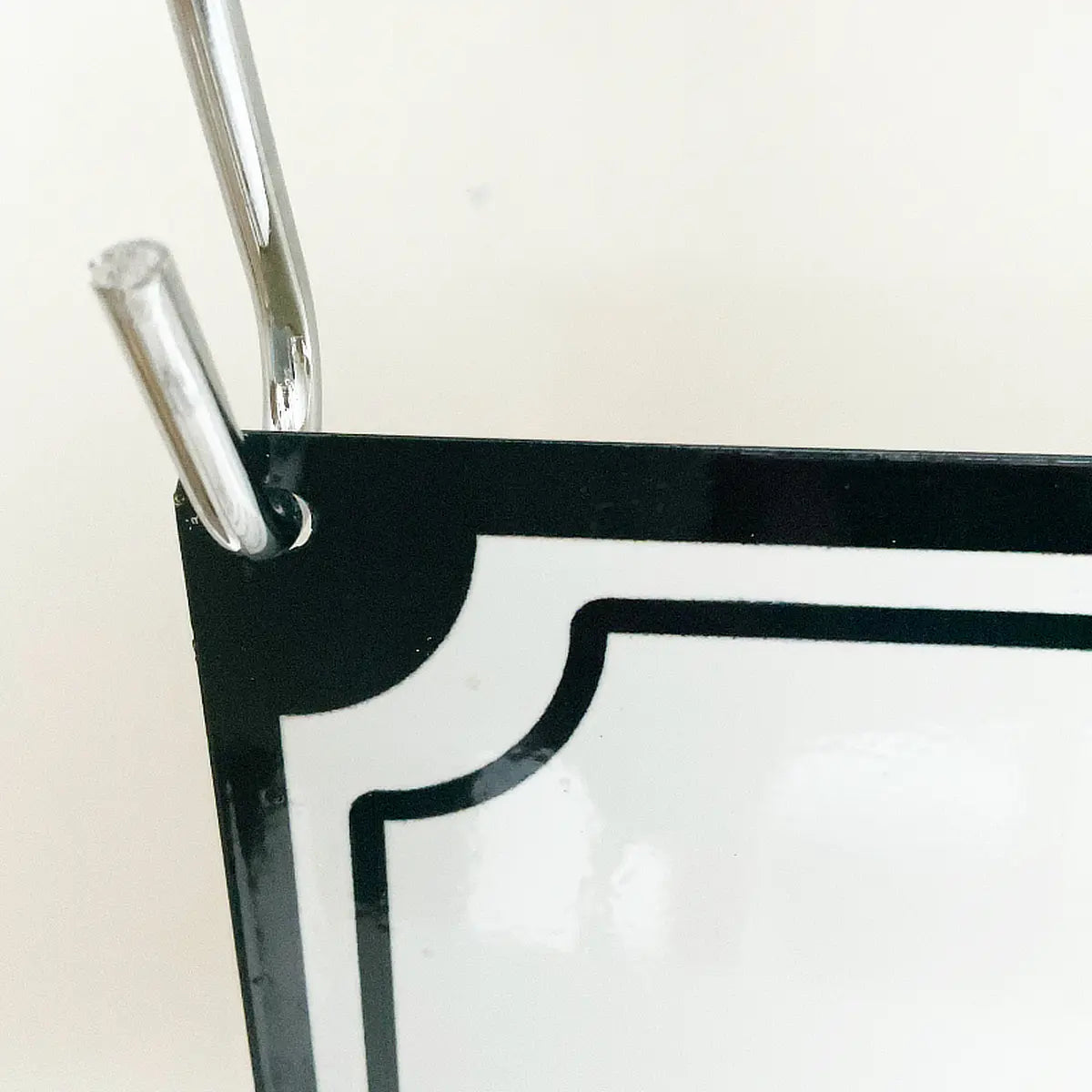 Close-up detail of metal S-hook hanging attachment on corner of gloss decorative sign