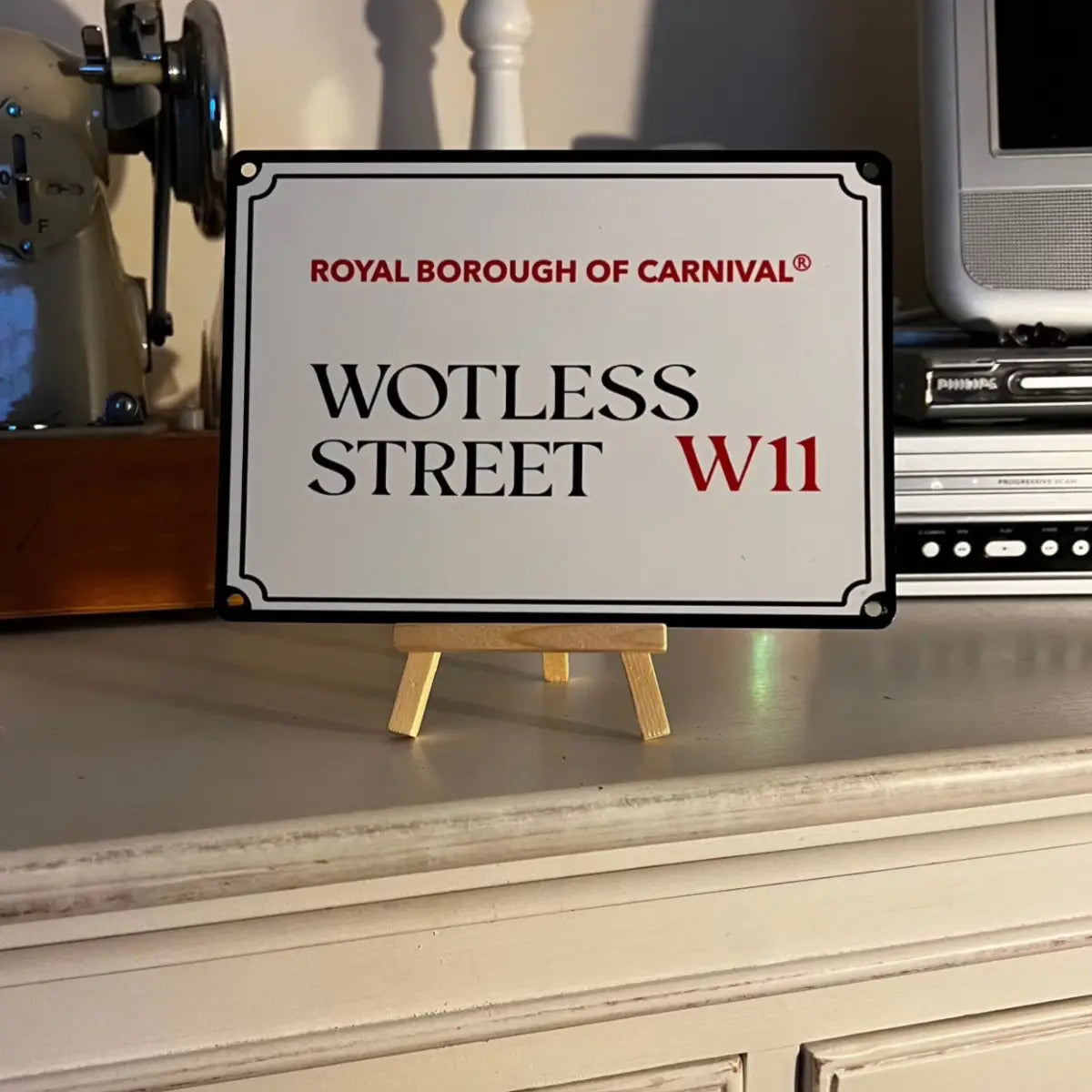 Wotless Street W11 decorative street sign displayed on a wooden easel atop a vintage painted chest of drawers