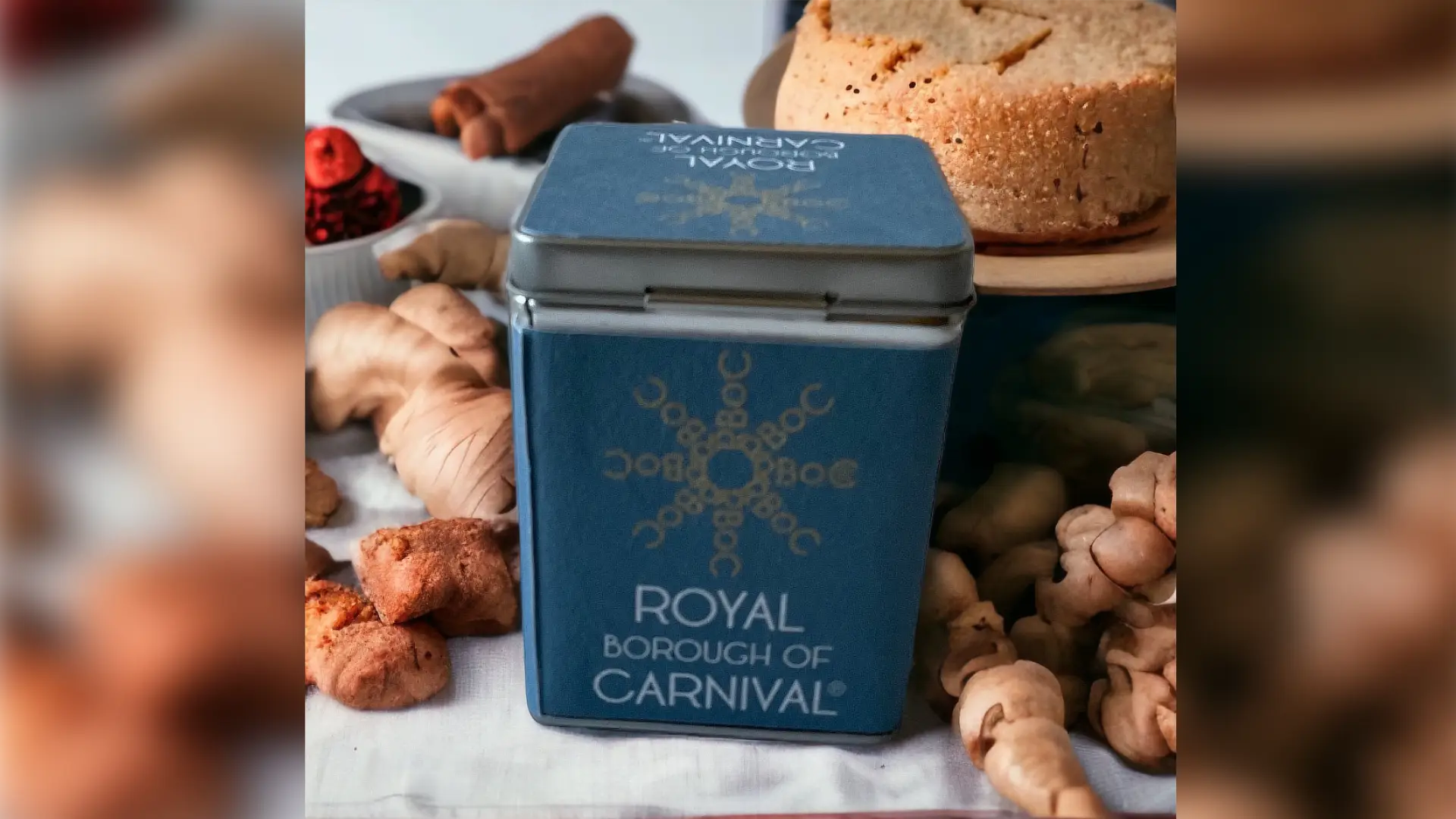 Royal Borough of Carnival branded blue tea caddy on a wooden tray with fresh ginger and cake.