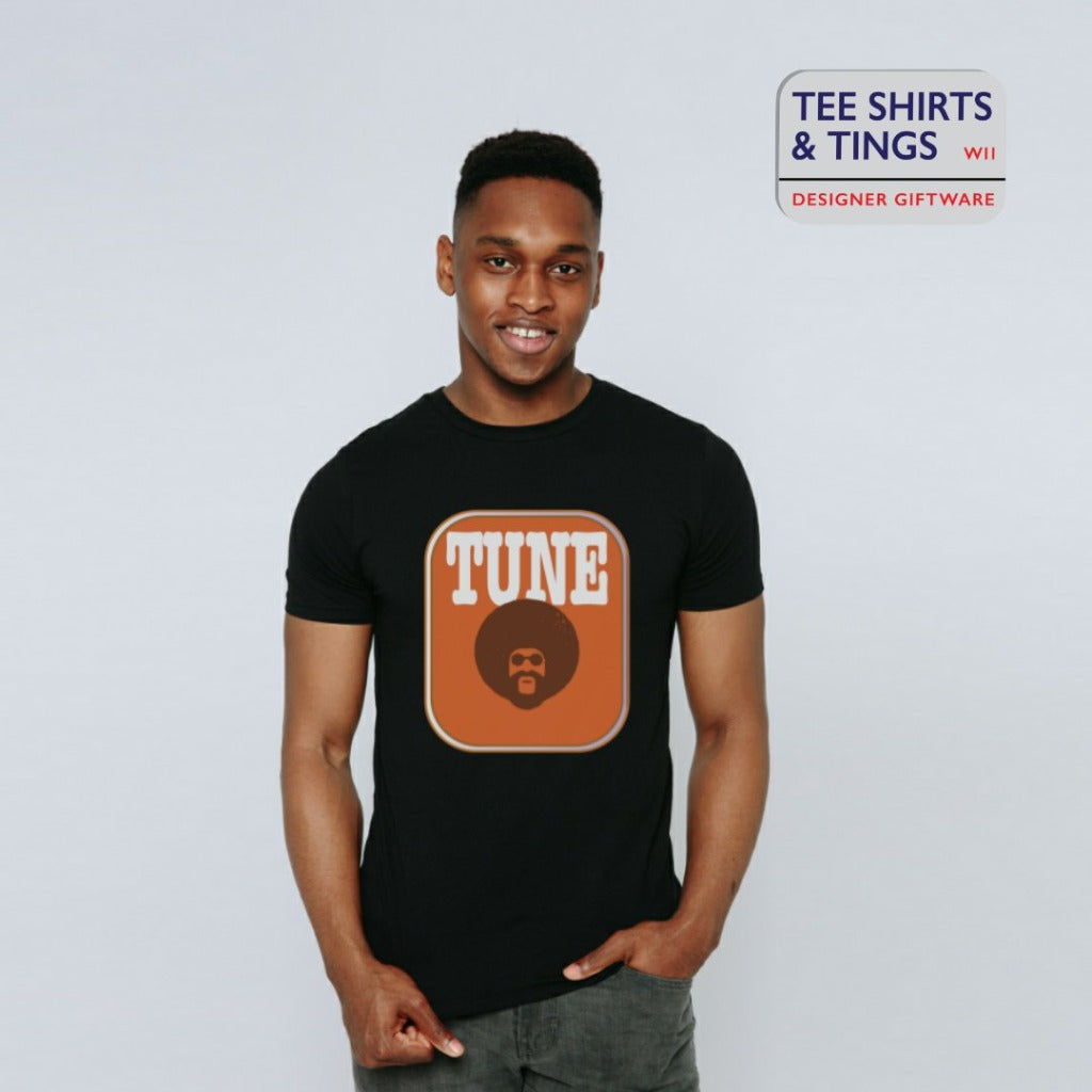 Young man in a studio wearing a black teeshirt with an amber rectangle on the front with an image of a man with afro hair and the wording in white saying TUNE. 100% organic cotton